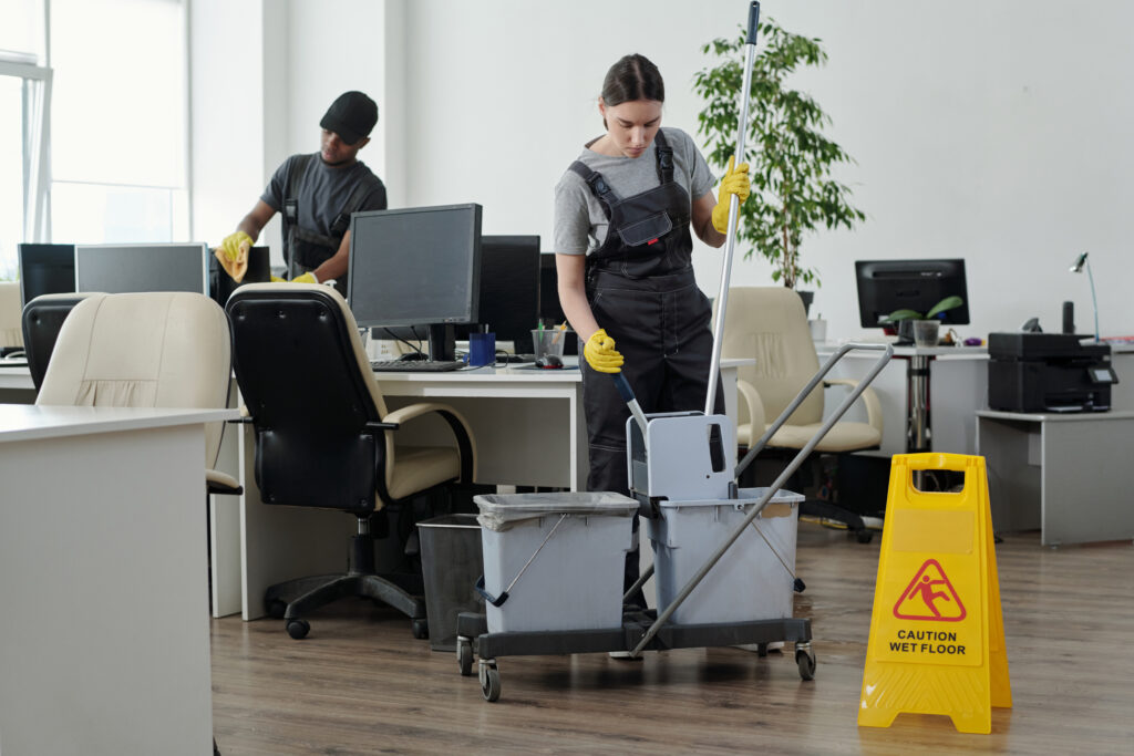 Young cleaning lady sqeezing mop in bucket while going to wash floor in office